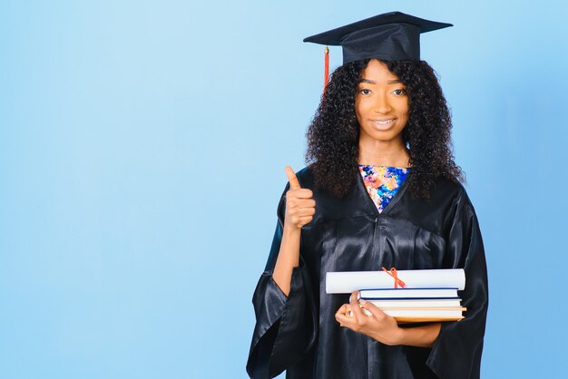 African-American beautiful woman in a black robe and hat, on a blue isolated background smiles.