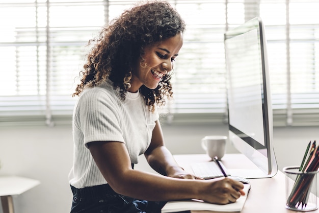 Donna di colore afroamericana che lavora con il computer portatile gente di affari creativa che progetta e che utilizza penna nel sottotetto del lavoro moderno