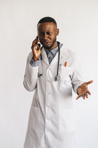 An African-American black young doctor in a white coat is talking on the phone