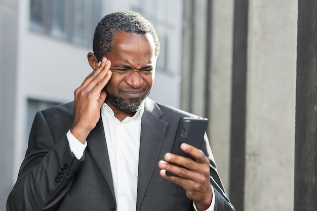 African american boss outside office building with phone in hands reading bad news online man