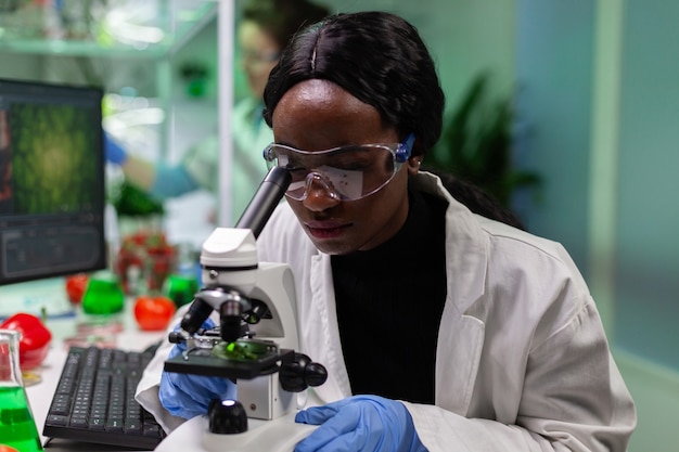 Photo african american botanist looking at leaf sample using medical microscope