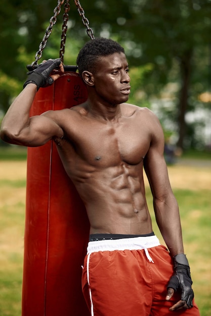 An african american boxer works with a punching bag, rests by a punching bag, trains in the city among the boxing grounds