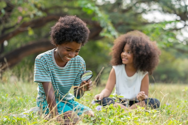 African American boy and girl sitting in grass exploring and looking nature with magnifying glass