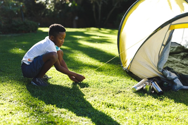 African american boy having fun pitching tent with ropes in sunny garden. spending time at home.