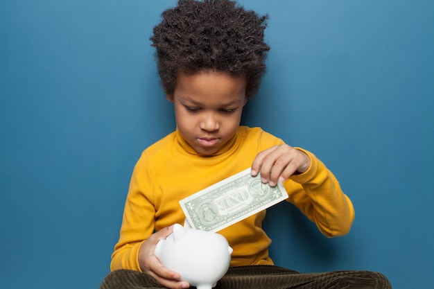 African American boy holding one us dollar and money box on blue background