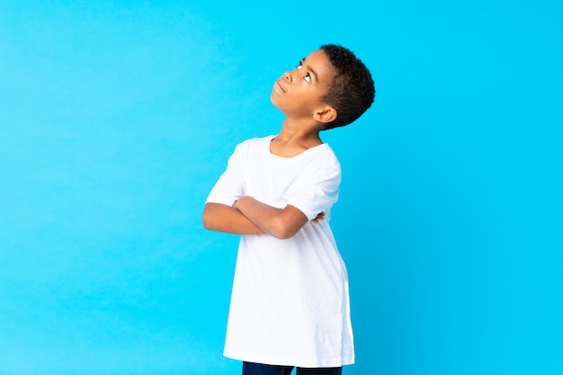 African American boy over isolated blue making doubts gesture while lifting the shoulders