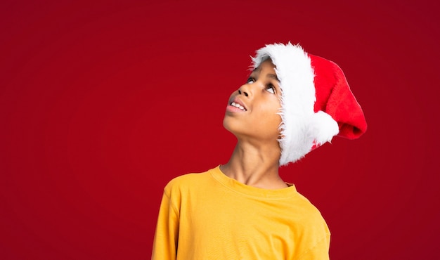 African American boy with christmas hat looking up while smiling over red wall