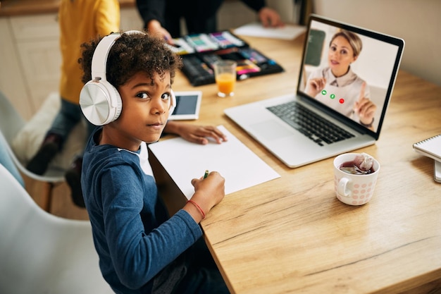 African American boy with headphones following online class over laptop from home