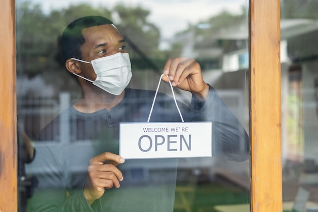 Photo african american business man with face mask holding the sign for the reopening and looking away of the place after lockdown quarantine small business owner reopen and back to new normal concept