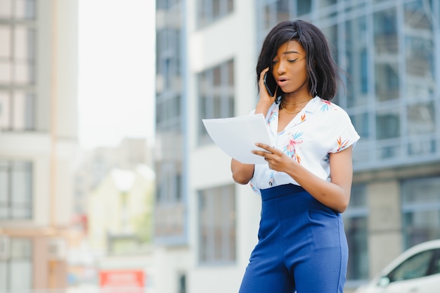 Donna afroamericana di affari che comunica su un telefono cellulare all'edificio per uffici