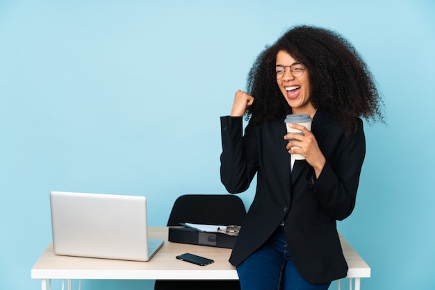 Афро-американская деловая женщина, работающая на своем рабочем месте, празднует победу