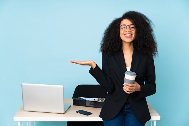 Donna afroamericana di affari che lavora nel suo posto di lavoro che tiene il copyspace immaginario sul palmo per inserire un annuncio