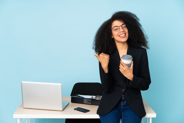 African american business woman working in her workplace pointing to the side to present a product