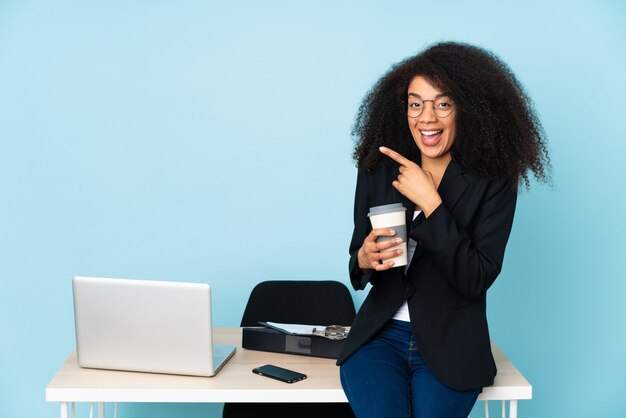 African american business woman working in her workplace surprised and pointing side