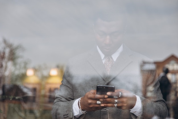 Uomo d'affari afroamericano in vestito grigio classico che tiene uno smartphone.