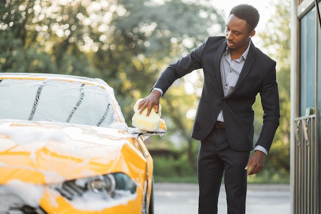 African American businessman in formal wear washing rearview car mirror