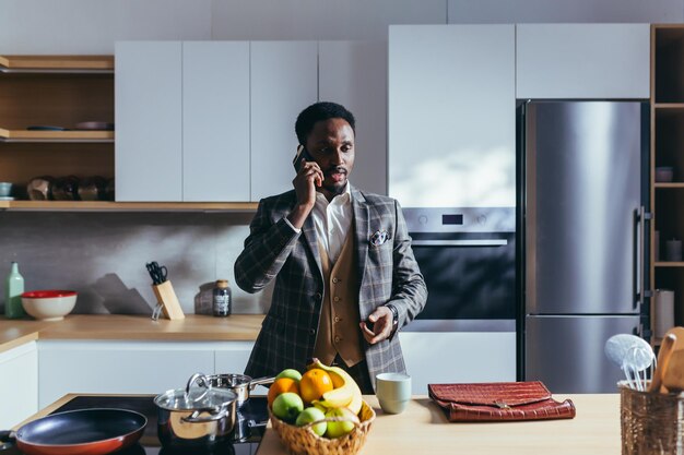 African American businessman going to work at home, having breakfast in the kitchen, talking on the phone