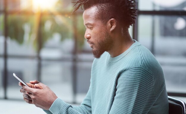 Афро-американский бизнесмен, использующий мобильные корпоративные приложения для телефона на рабочем месте, отправляет смс