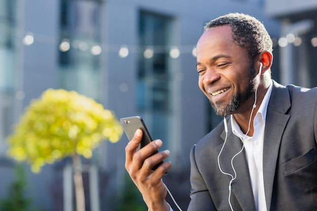 African american businessman using phone sitting on bench outside office building boss watching