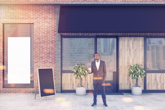 Photo african american businessman with a coffee to go standing near a brick and wooden modern restaurant. 3d rendering mock up toned image