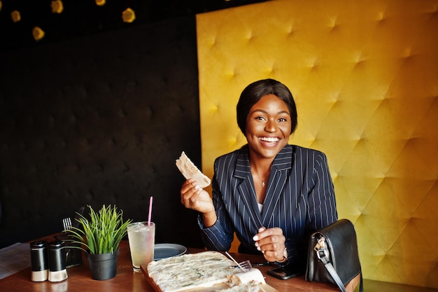 African american businesswoman eating cheese pizza in cafe Black girl having rest