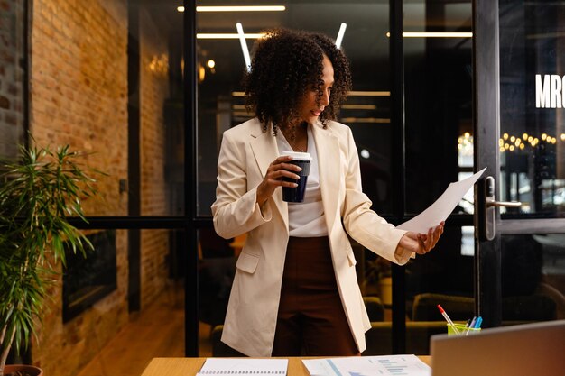 Photo african american casual businesswoman with cup of coffee reading document in office. casual office, business, professional and work, unaltered.