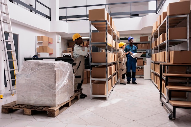 African american and caucasian warehouse workers scanning parcels barcodes and making inventory. Diverse delivery service storage employees team wearing uniform working in storehouse