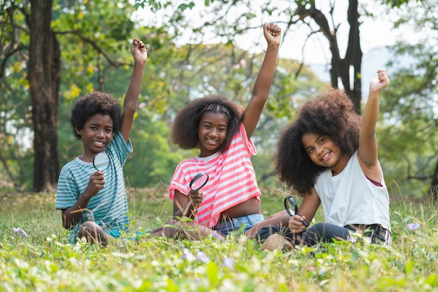 African American children sitting in the grass and looking through the magnifying glass