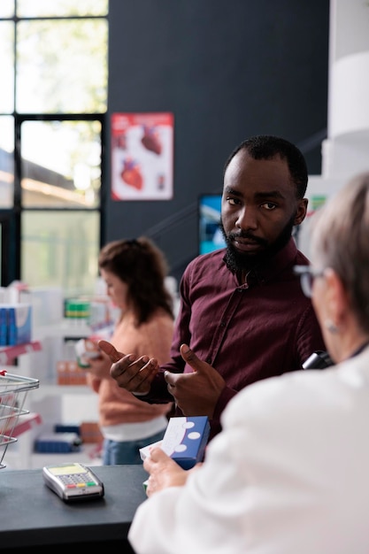 African american client asking pharmacist for help with medicaments prescription discussing health care treatment in pharmacy. Drugstore worker offering support assistance to clients, medicine service