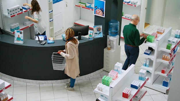 African american client buying pharmaceutical products and\
medicaments at drugstore counter, talking to pharmacist about\
medicine and drugs. woman paying for supplements at pharmacy.