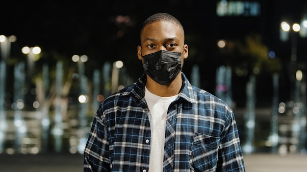 Photo african american confident male man guy wears medical mask standing in night city looking at camera