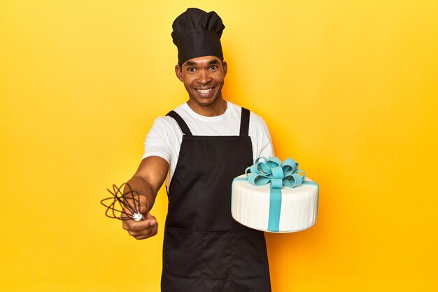 African American cook holding a freshly baked cake in a yellow studio