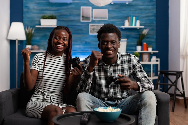 African american couple being happy for winning game on console\
sitting on sofa at home. boyfriend and girlfriend excited over\
victory on video game played together in living room