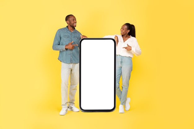 African American Couple Pointing At Cellphone Screen On Yellow Background