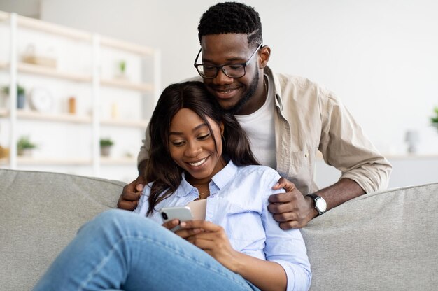 African american couple sitting on couch using mobile phone