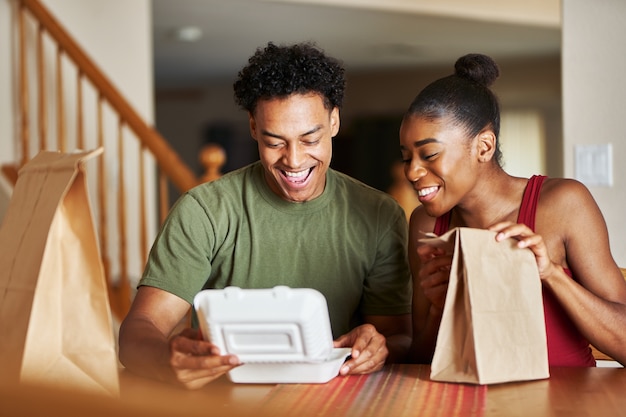 African american couple sitting at table looking at food delivery