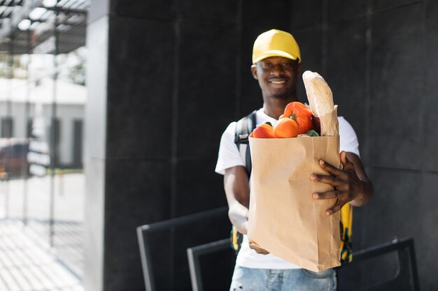 African American courier standing with a package with fresh food from the store