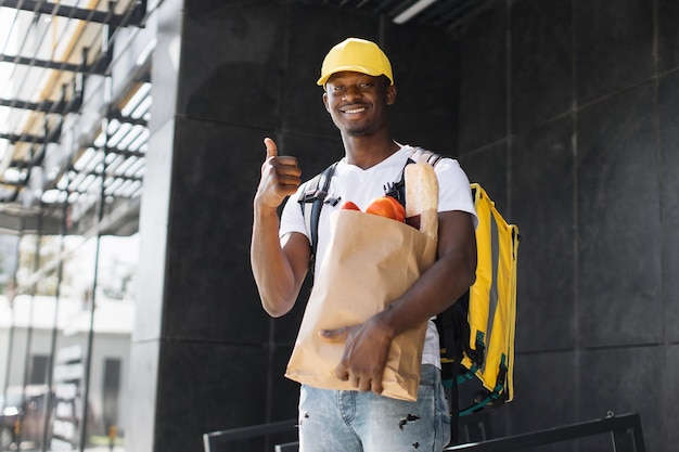 African American courier standing with a package with fresh food from the store