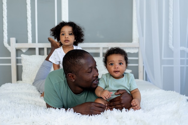 아프리카 계 미국인 아빠가 침실에있는 침대에서 집에서 아이들과 놀다가 아버지의 사랑을 껴안고