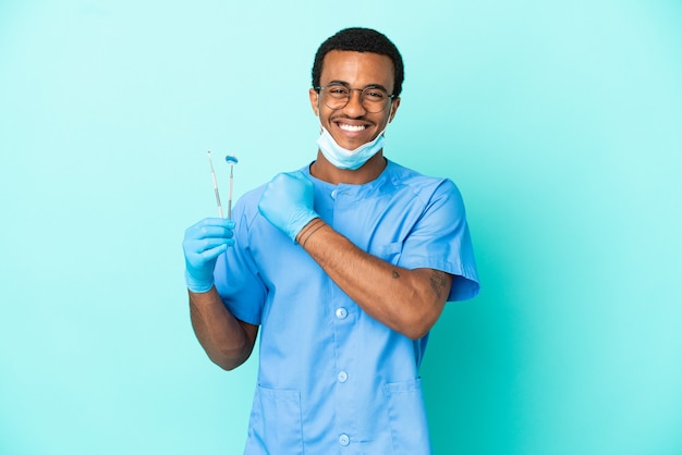 African American dentist holding tools over isolated blue background celebrating a victory