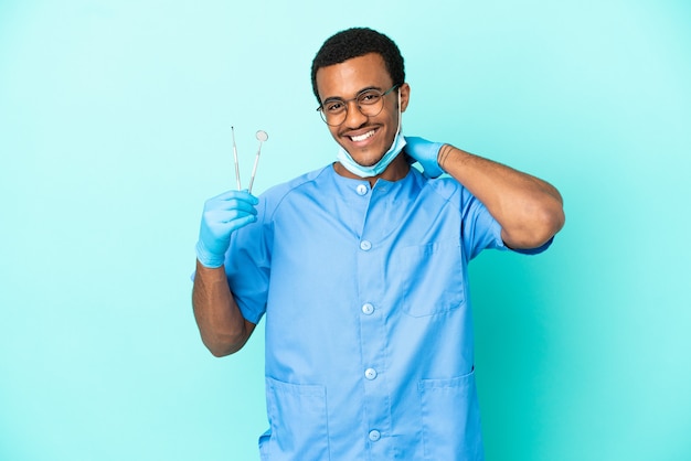 Афро-американский дантист держит инструменты на синем фоне, смеясь