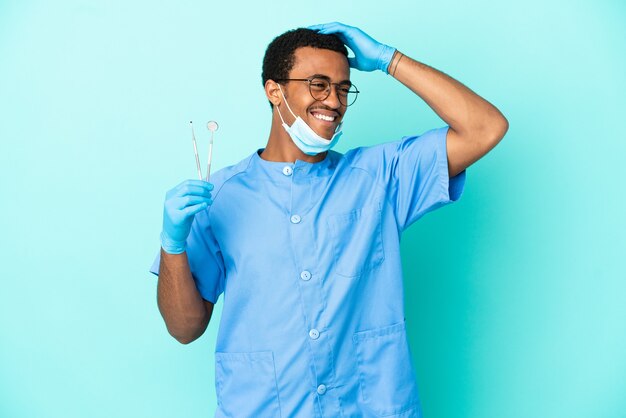 たくさん笑って孤立した青い背景の上にツールを保持しているアフリカ系アメリカ人の歯科医
