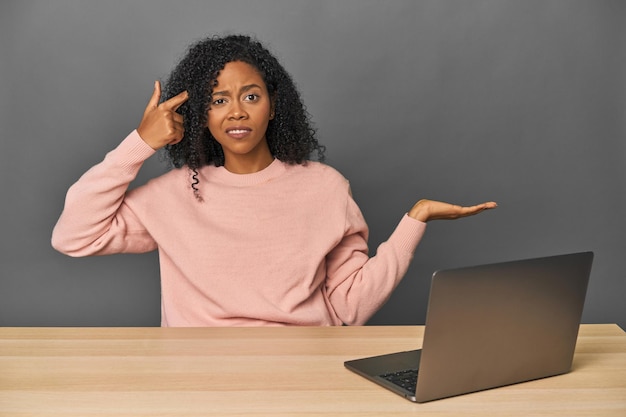 Photo african american at desk with laptop holding and showing a product on hand