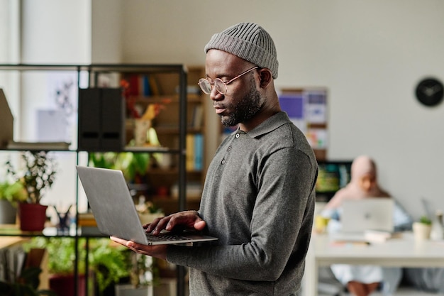 사무실에 서있는 동안 노트북에 입력하는 아프리카 계 미국인 개발자