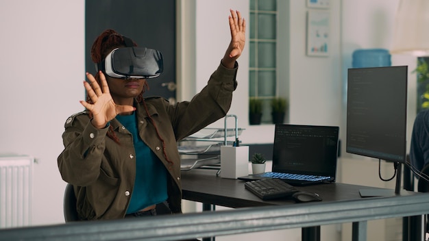 African american developer working with vr glasses to create programming server with html script on terminal window. System engineer using virtual reality headset to plan new interface.