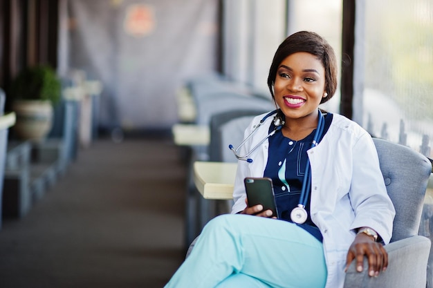 Foto la donna afroamericana del medico con lo stetoscopio ha guardato il telefono e si è seduta sulla clinica
