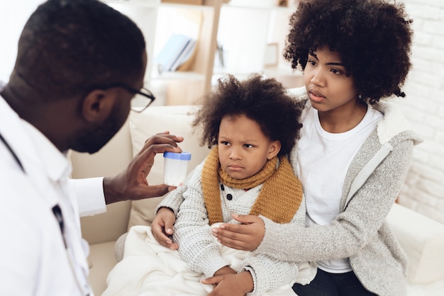 African American doctor gives pills to sick kid with flu.