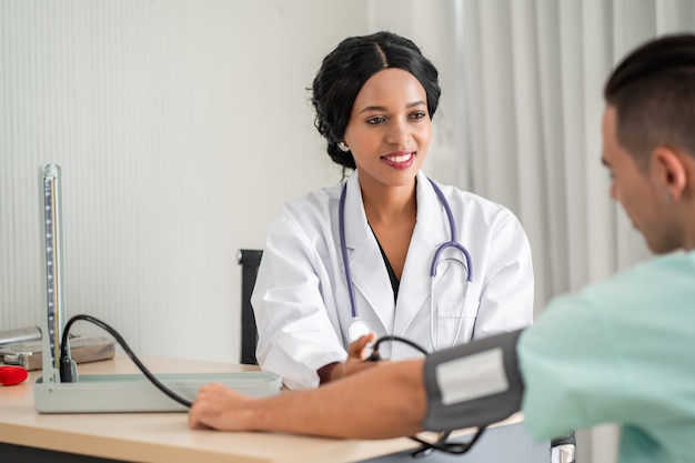 The african american doctor is measuring blood pressure for the patient. And provide consultation regarding treatment to patients sitting in a wheelchair and closely monitor