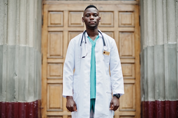 African american doctor male at lab coat with stethoscope outdoor against clinic door.