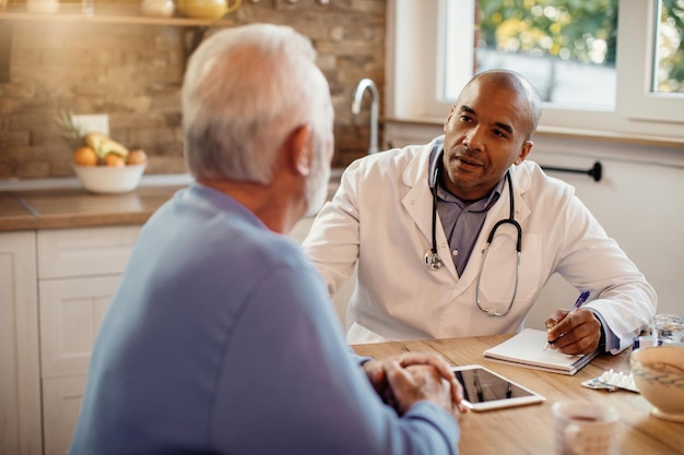 Medico afroamericano che parla con un uomo anziano mentre lo visita a casa